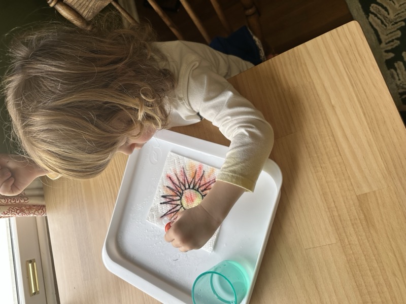Young child coloring a paper towel during a simple water-play activity