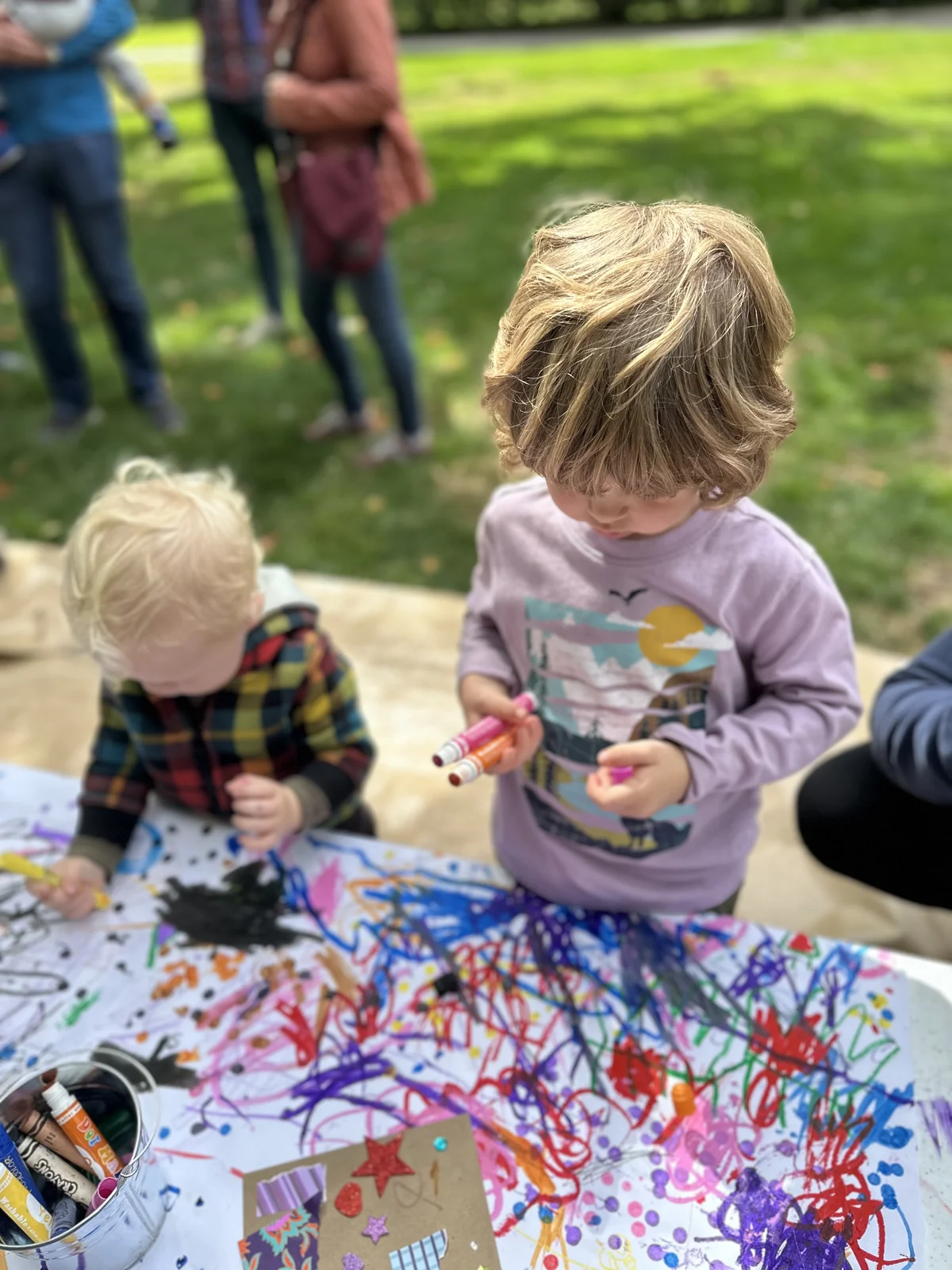 Two young children drawing together outdoors with colorful markers